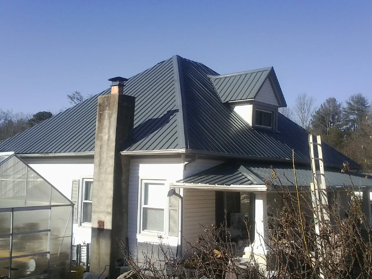 Dark blue standing seam metal roof on a white farmhouse with dormer — Slate & Tile Roof Repair by Roofing Brothers in Black Creek