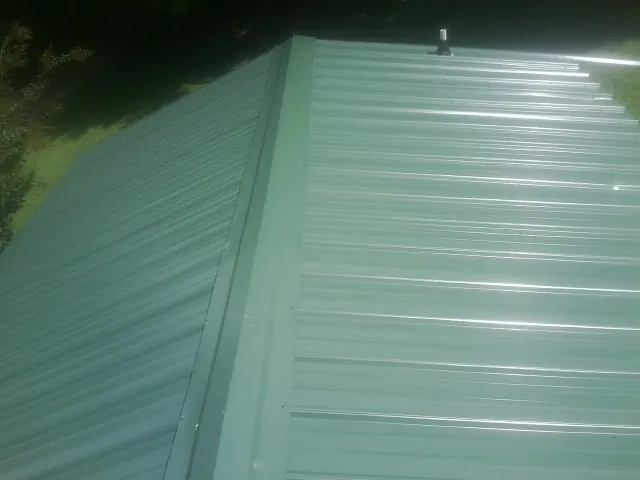 New green metal panels meeting at the ridge of a roof — Flat Roof Repair work by our crew in Black Creek
