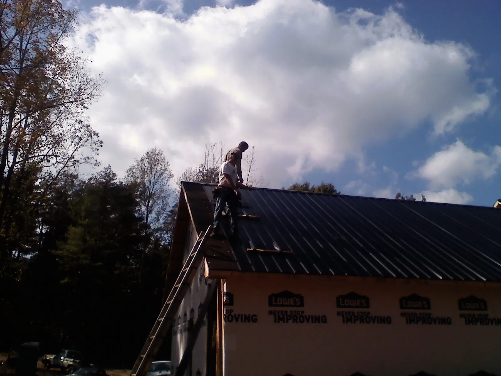 Roofer fastening dark metal panels high against a cloudy sky, from a Roof Inspection job in Black Creek