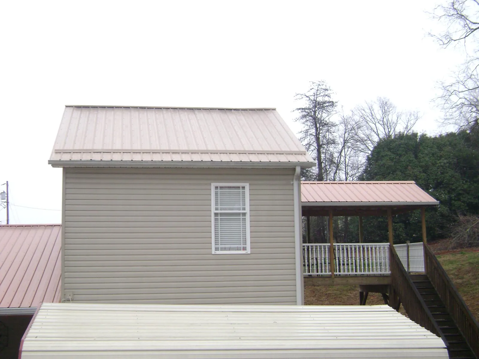 Tan metal roofs on a two story addition and attached porch, from a Roof Replacement job in Black Creek